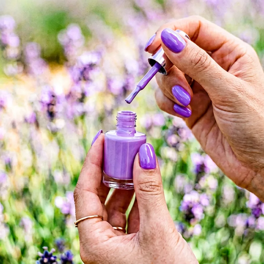 Hand applying lavender gel polish under an LED lamp during a home manicure